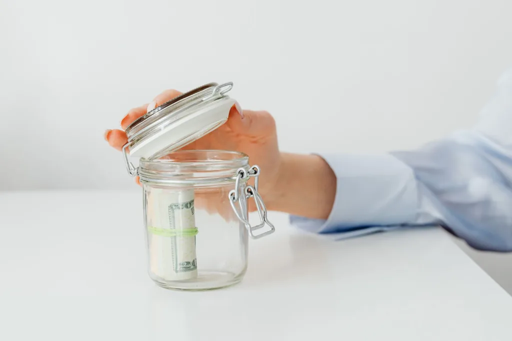 Hand putting cash into a glass jar to grow savings in a high-yield savings account