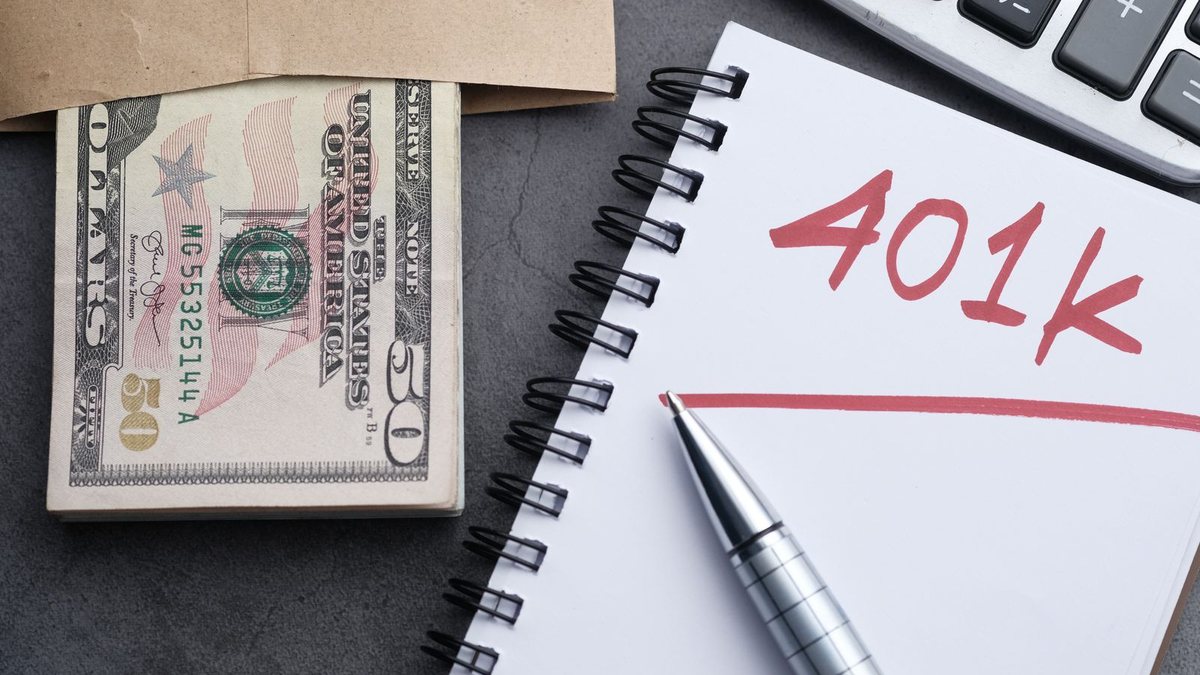 Notebook with 401k written in red next to a pen, a calculator and an envelope of US dollar bills