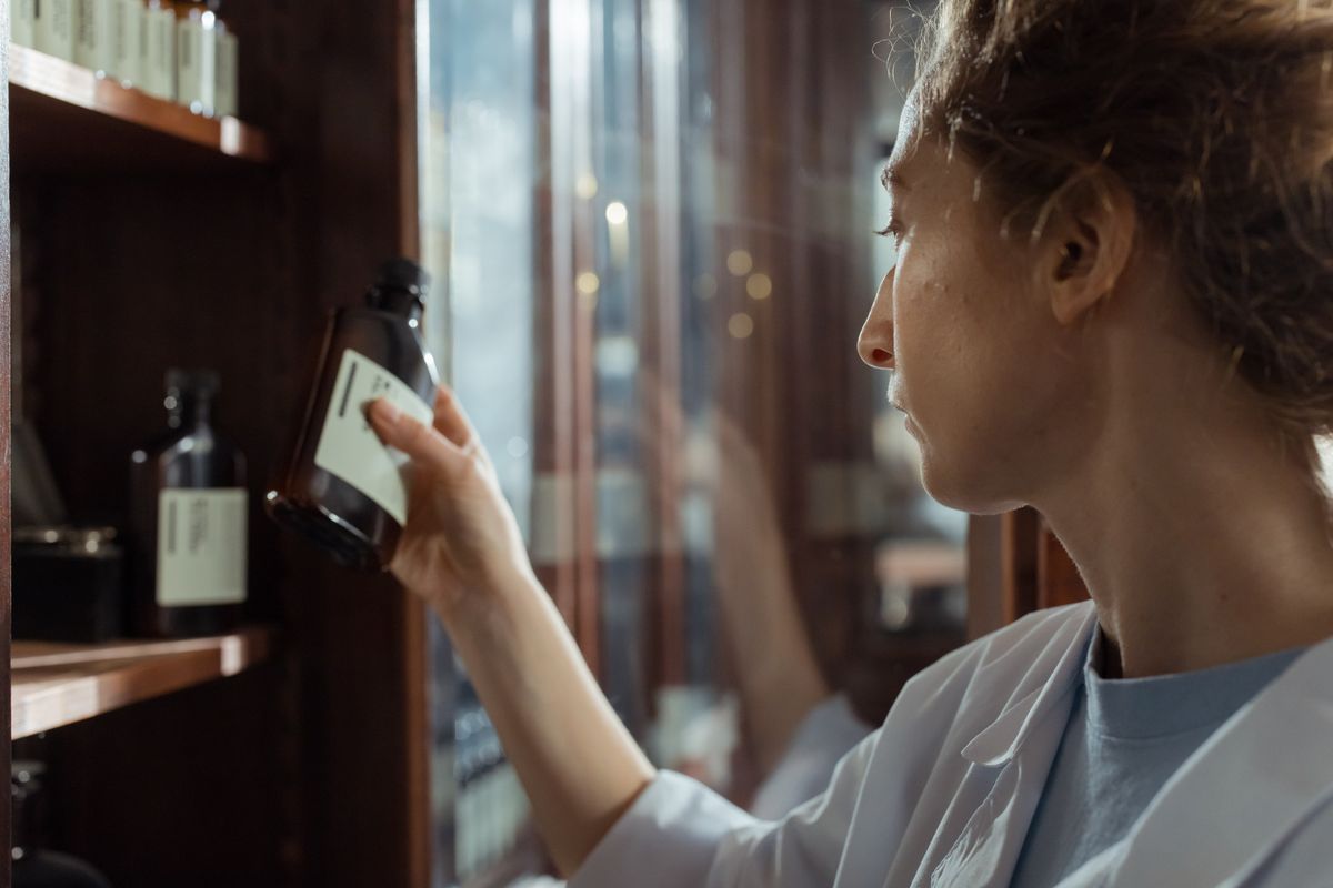 Pharmacist in a white coat checking a medicine bottle on a pharmacy shelf