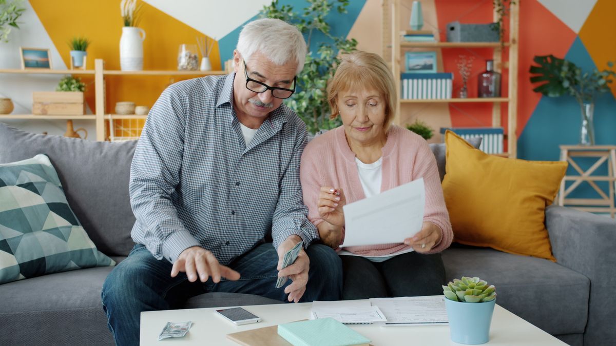 Senior couple sitting on a sofa reviewing household bills and savings paperwork