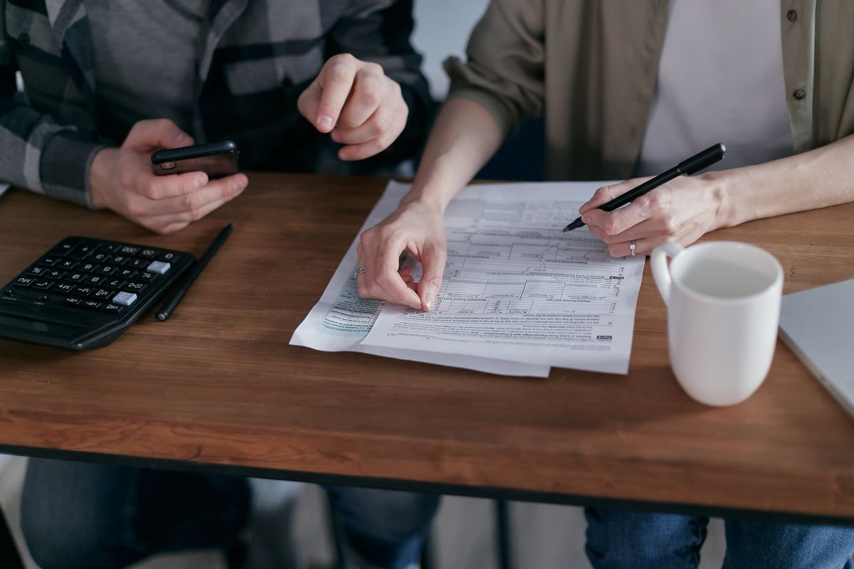 Couple reviewing tax forms with a calculator and smartphone at a wooden table